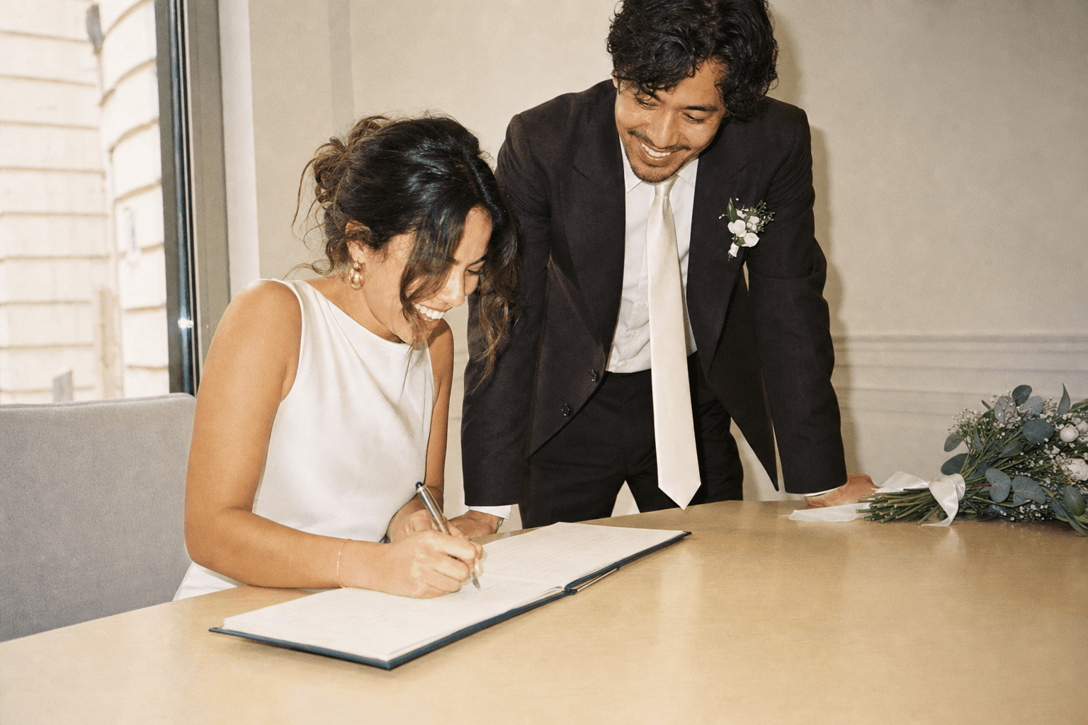 The bride signing the wedding register while the groom watches